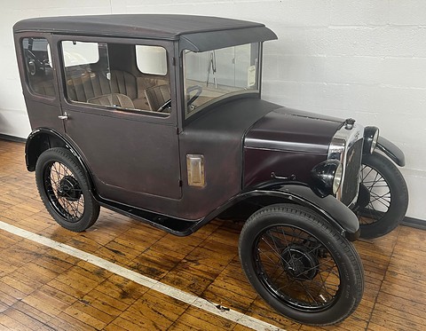 A grey fabric-covered small saloon with black wire wheels on a wooden museum floor.