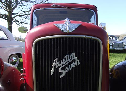 A red bonnet with a winged mascot above a black mesh grille carrying the words Austin Seven in chrome script. Opens a larger view