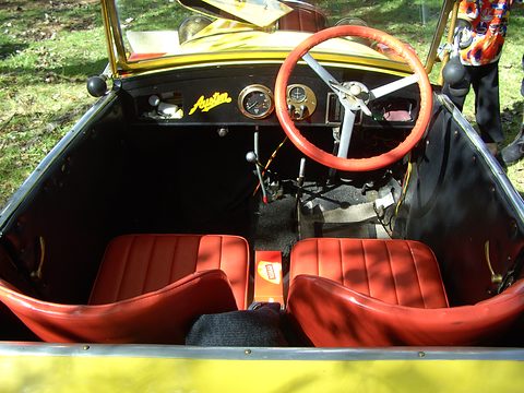 Looking into a small open car over red leather seats to a cream steering wheel and a wooden dashboard. Opens a larger view
