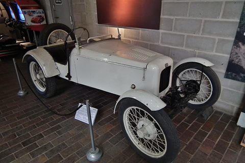 A white bodiless trials special with wire wheels on a brick floor beside a display stand. Opens a larger view