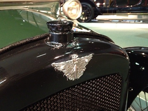 A black radiator top with a round cap and a chrome winged badge over the honeycomb. Opens a larger view