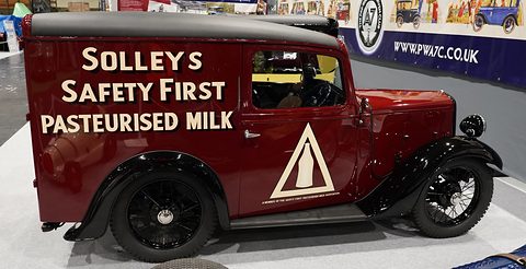 A dark red van with white lettering for pasteurised milk and a triangle sign on its side, on a show stand. Opens a larger view