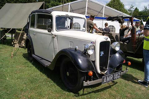 A cream-bodied cabriolet with black wings and its hood up, on grass beside marquees and visitors. Opens a larger view