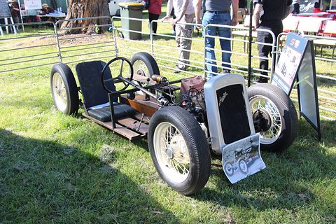 A stripped Austin Seven chassis with a radiator, seat and four wheels but no body, parked on grass. Opens a larger view