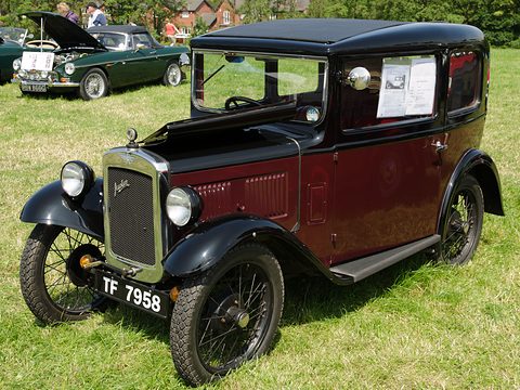A maroon and black square saloon with wire wheels and a notice on its window, on grass. Opens a larger view