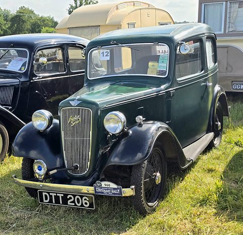 A dark green rounded saloon with a cowled chrome grille and black wheels on grass beside other cars. Opens a larger view