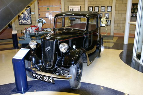 A black rounded saloon on a museum floor beside a blue display stand. Opens a larger view