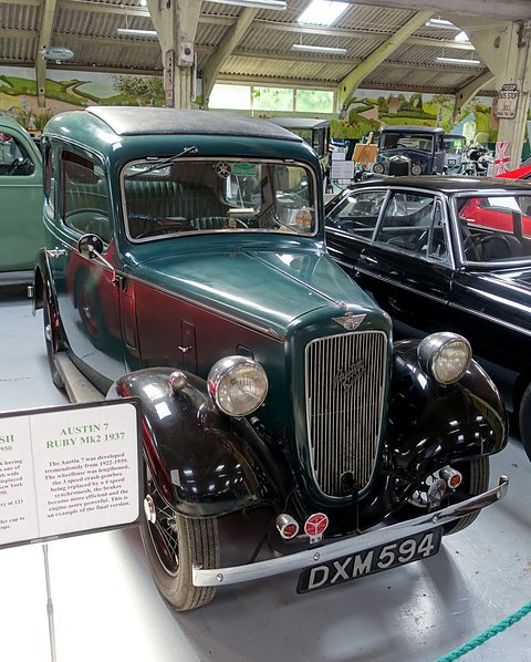 A green and black rounded saloon behind a rope in a museum, a display card beside it. Opens a larger view
