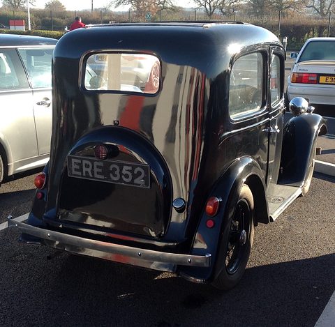 The rounded rear of a dark blue saloon with a spare-wheel cover and number plate, in a car park. Opens a larger view