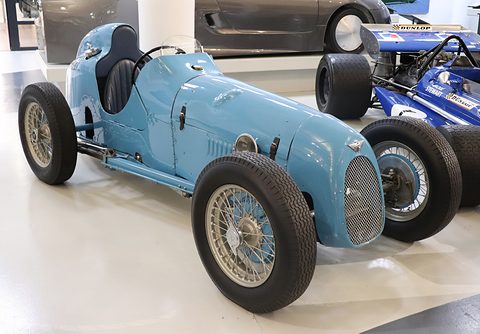 A pale blue streamlined single-seat racing car with wire wheels on a white museum floor. Opens a larger view