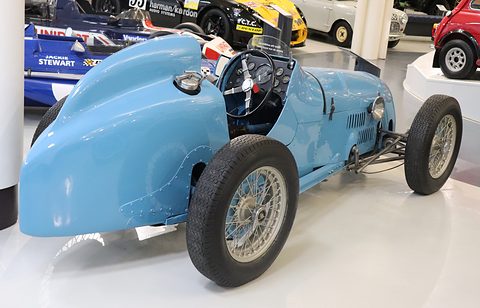 The rear of a pale blue single-seater with a long rounded tail and wire wheels. Opens a larger view