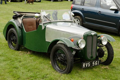 A green two-seater with an aluminium bonnet, brown seats and wire wheels on grass. Opens a larger view