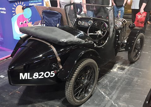 The pointed black tail of a sports two-seater with a strap across it and a number plate. Opens a larger view