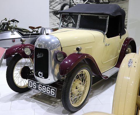 A cream two-seater with maroon wings, a polished radiator cowl and wire wheels with its hood up. Opens a larger view