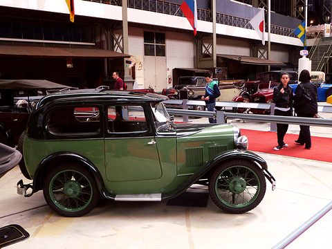 A green two-tone saloon with wire wheels on a white floor in a large exhibition hall. Opens a larger view