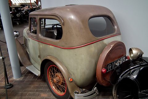 The rear of a weathered brown saloon with faded paint, orange wheels and a spare wheel. Opens a larger view