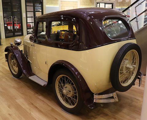 The rear of a cream saloon with a brown roof and a spare wheel on its tail, on a wooden floor. Opens a larger view