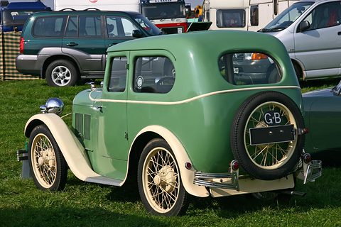 The rear quarter of a green saloon with cream wings, wire wheels and a GB plate on the spare wheel. Opens a larger view