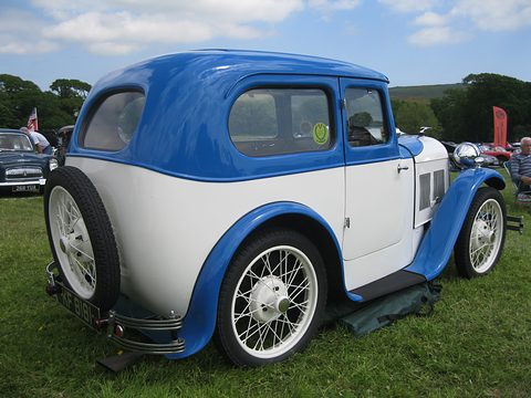 The rear quarter of a white saloon with a blue domed roof and wings and a spare wheel at the back. Opens a larger view