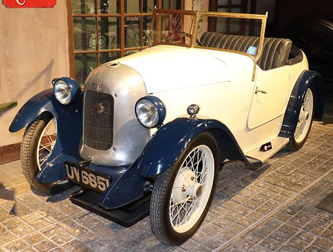 A cream two-seater with dark blue wings, a polished cowl and wire wheels on a stone floor. Opens a larger view