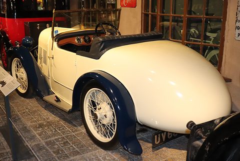 The rear of a cream two-seater with a long rounded tail and blue wings in a museum. Opens a larger view