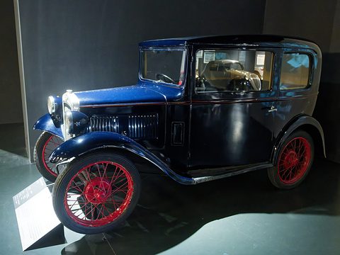 A dark blue and black square saloon with red wire wheels under spotlights against a dark wall. Opens a larger view