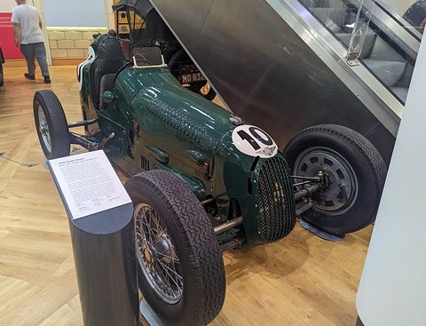 A dark green single-seat racer, number 10, with its engine cover raised and a display panel beside it. Opens a larger view
