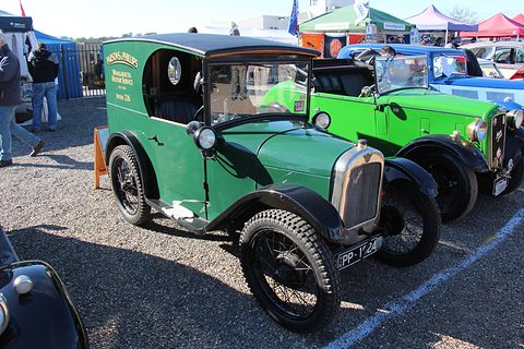 A green van with black wings and wire wheels in a car park, other green cars beside it. Opens a larger view