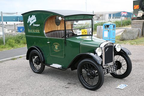 A dark green van with gold lettering, black wings and wire wheels in a car park. Opens a larger view