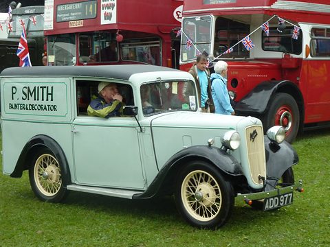 A pale green van lettered P. Smith Painter and Decorator on grass by red London buses. Opens a larger view