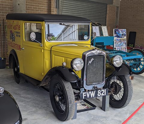 A yellow van with black roof and wings and lettering on its side, parked in a brick museum hall. Opens a larger view