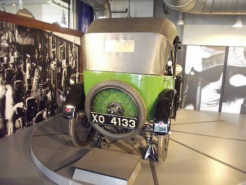 The rear of a green open tourer with a fabric hood, a spare wheel and number plate XO 4133. Opens a larger view