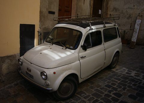 White small estate car with a rusty roof rack parked in a shaded cobbled lane. Opens a larger view