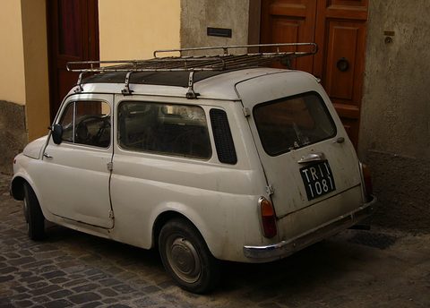 Rear of a white small estate car with a roof rack parked on cobbles before old wooden doors. Opens a larger view
