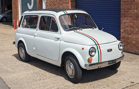 White small estate car with green, white and red stripes parked before a brick wall and a blue shutter. Opens a larger view