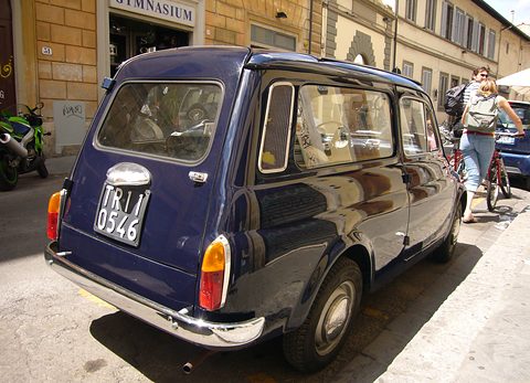 Rear of a dark blue small estate car parked in a sunny street, a cyclist passing behind. Opens a larger view