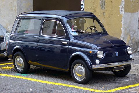 Dark blue small estate car parked in a yellow-marked bay before an ochre wall. Opens a larger view
