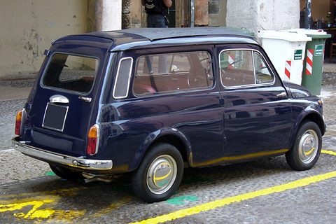 Rear of a dark blue small estate car with pillar air grilles, parked by bins in a yellow bay. Opens a larger view