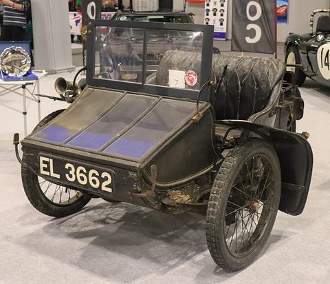 Front of a black three-wheeled vehicle with a lidded box between two wheels and a windscreen behind.