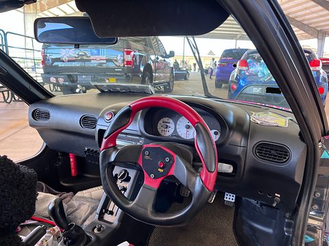 Black dashboard with round dials and a red and black aftermarket steering wheel, seen through the raised gullwing door. Opens a larger view