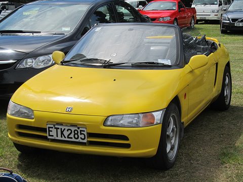 Yellow small open two-seater with an ETK285 plate parked on grass beside a dark saloon. Opens a larger view
