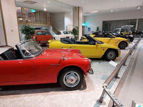 Two small yellow roadsters lined up in a museum hall behind a red open roadster in the foreground. Opens a larger view
