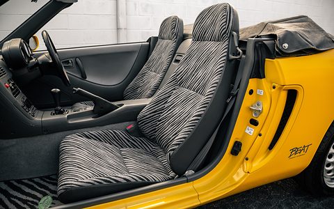 Two black and grey zebra-striped seats inside a yellow open car, seen through the open door with BEAT script. Opens a larger view