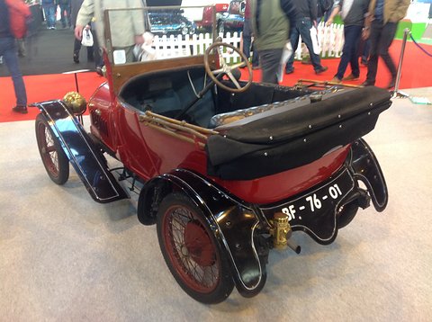 Red two-seater with black wings, folded black hood and French plate BF-76-01 on a grey carpet. Opens a larger view