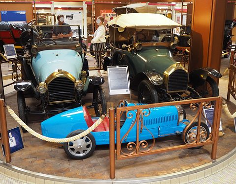 Two small open veteran cars, one light blue and one green, behind a blue child’s racing car and a rope barrier. Opens a larger view
