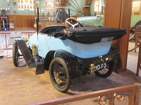 Back of a light blue two-seater with a folded black hood and plate 10-F3 on a brick floor. Opens a larger view