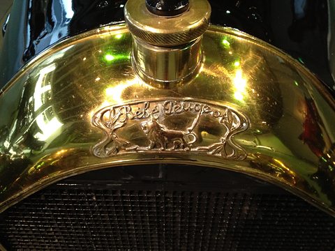 Close-up of a polished brass radiator shell with a filler cap and an ornate lion badge. Opens a larger view