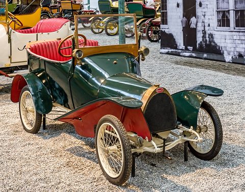 Dark green and red two-seater with a pointed radiator, wire wheels and red seats on pale gravel.