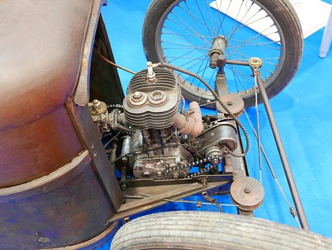 Close view of a small single-cylinder engine with a finned cylinder and a pulley beside a wire wheel. Opens a larger view
