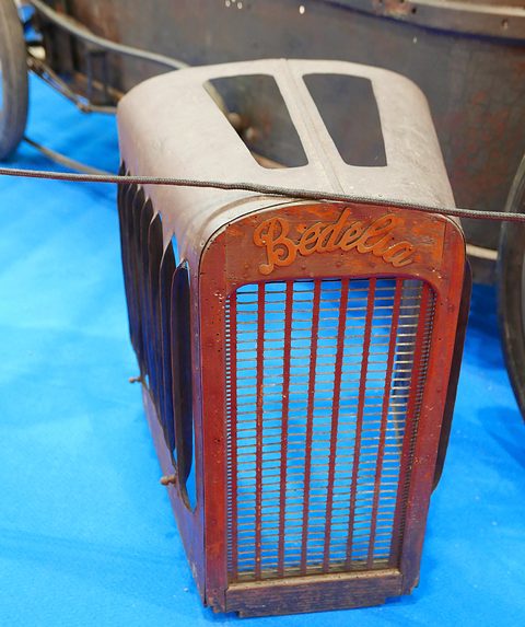 Close view of a rusty radiator cowl with a script badge and vertical slats. Opens a larger view